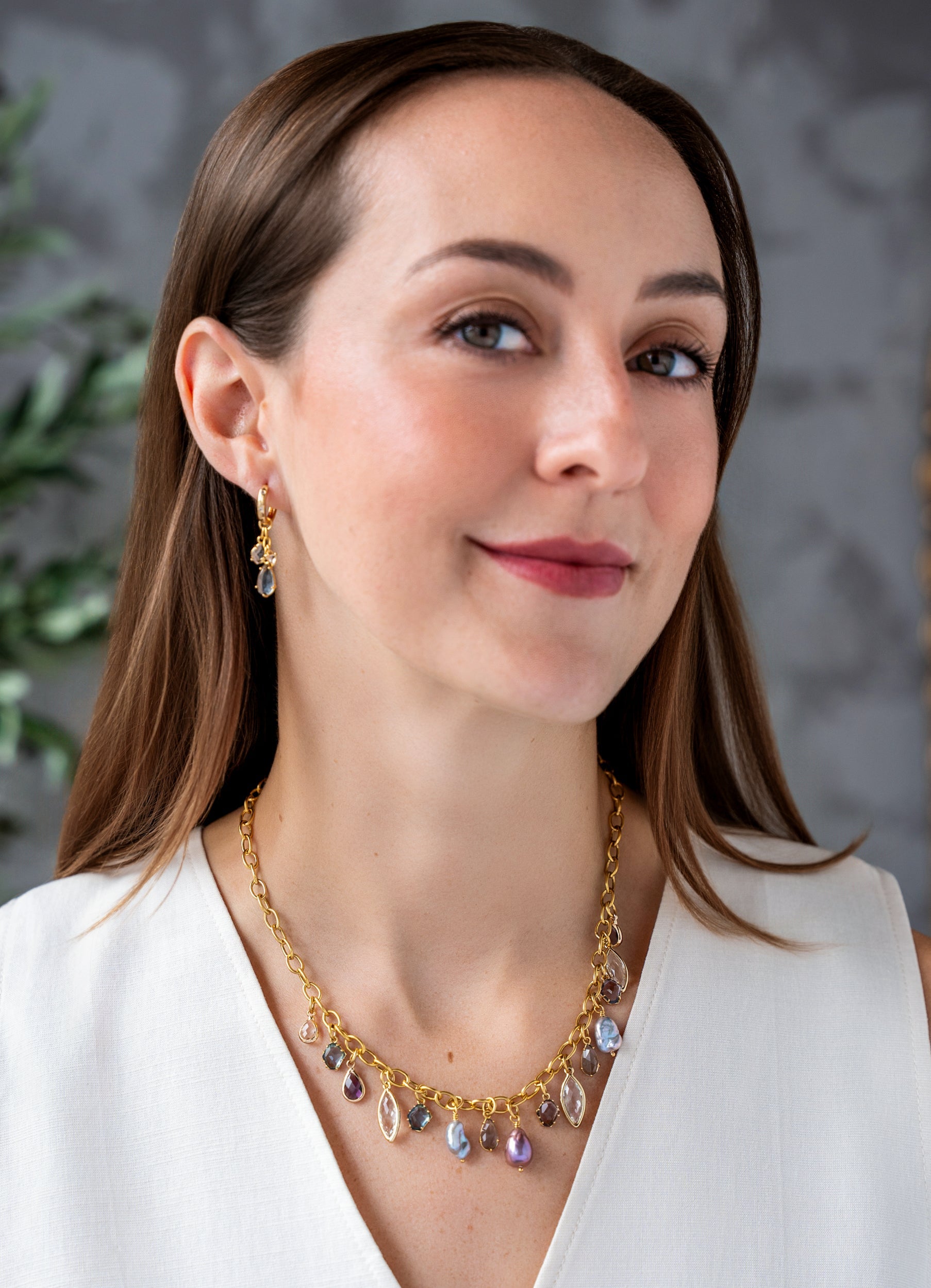 Gold charm necklace with colorful faceted gemstone charms and freshwater pearls dangling from an elongated gold chain.