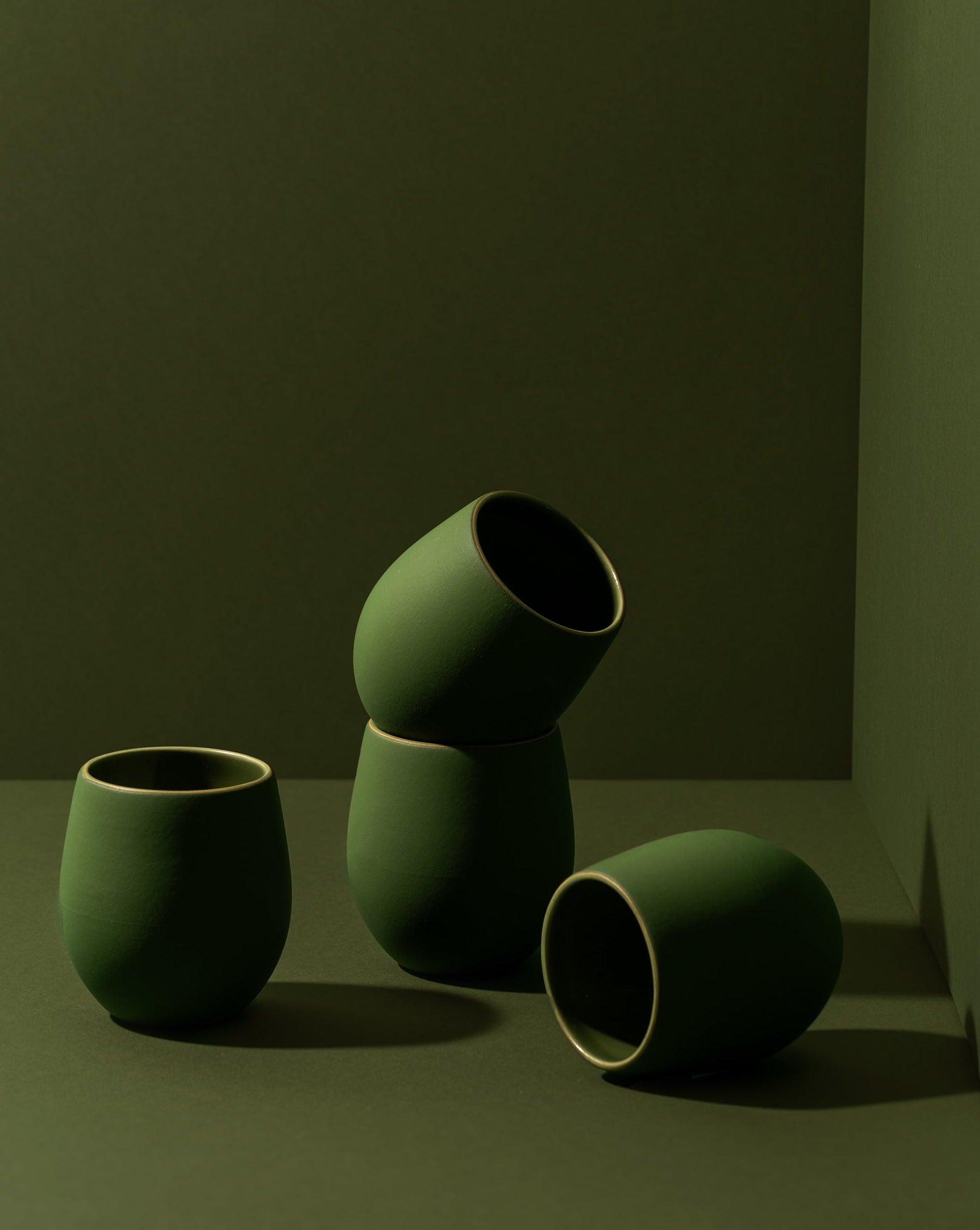 A set of four stoneware coffee cups arranged in a casual manner, with a matte green finish.