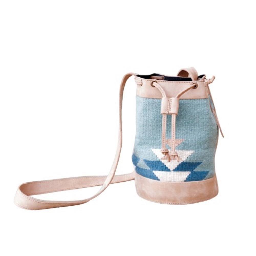 Handwoven blue wool and leather cinched bucket bag with adjustable strap, featuring a soft silhouette inspired by river currents; artisan-made and spacious.