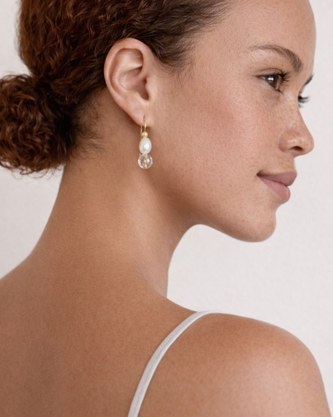Close-up of a woman wearing pearl earrings with a neutral background