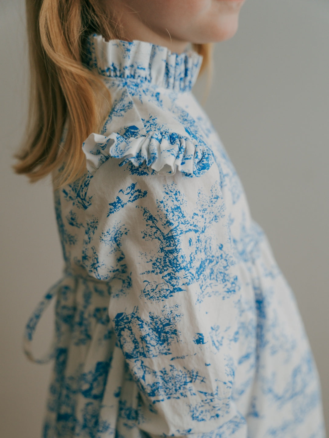 Close-up of a girl wearing a blue toile floral dress with ruffled sleeves.