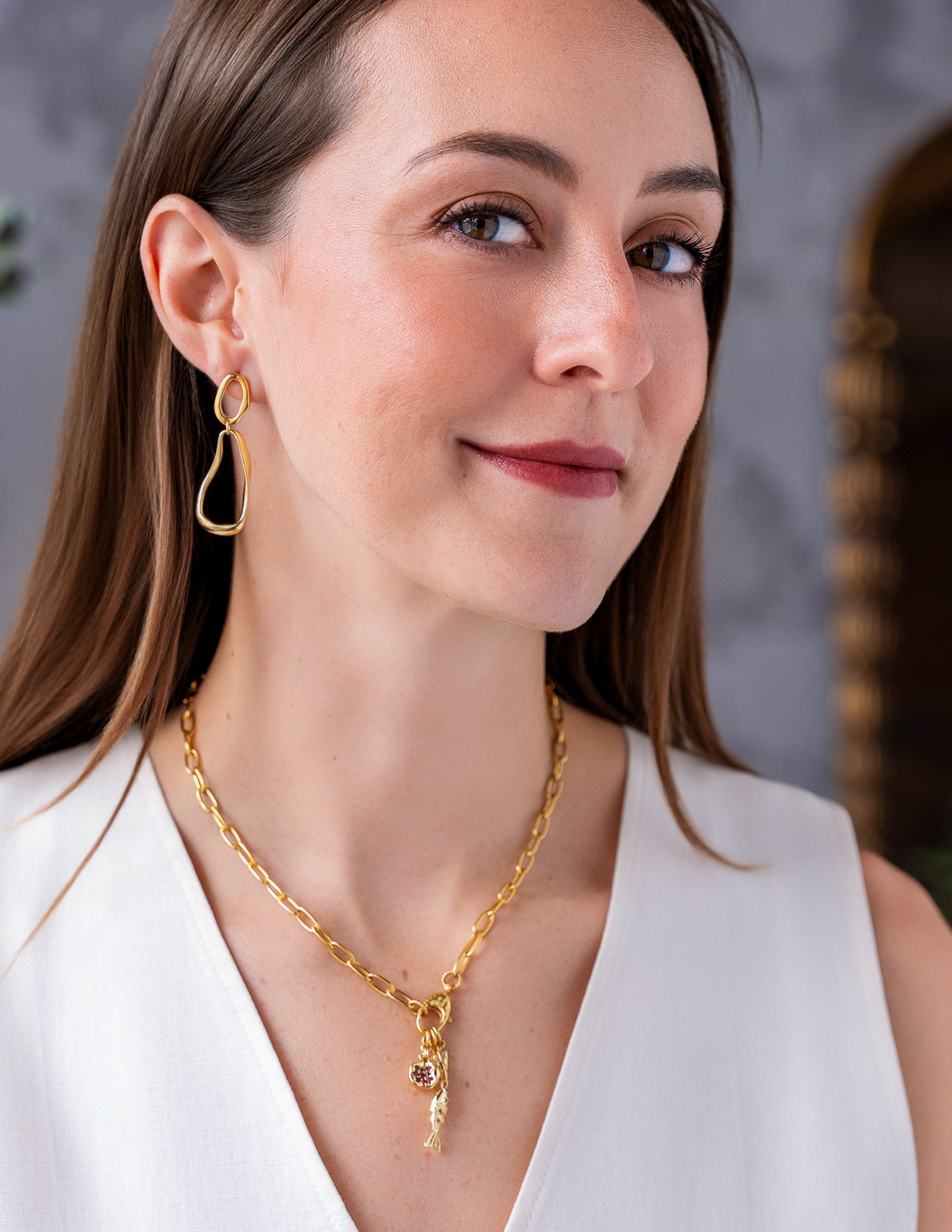 Gold chain necklace with fish charm, pomegranate charm, and crystal accents.