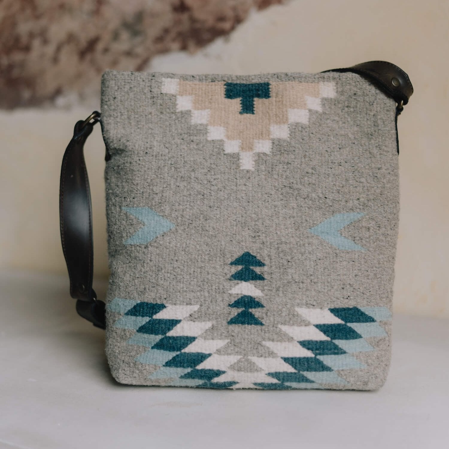 Side view AMASOUK handwoven wool Aguila Shoulder/Crossbody bag in a Zapotec pattern with blue, ivory, and honey on a gray background. Effortlessly stylish for day-to-night use.