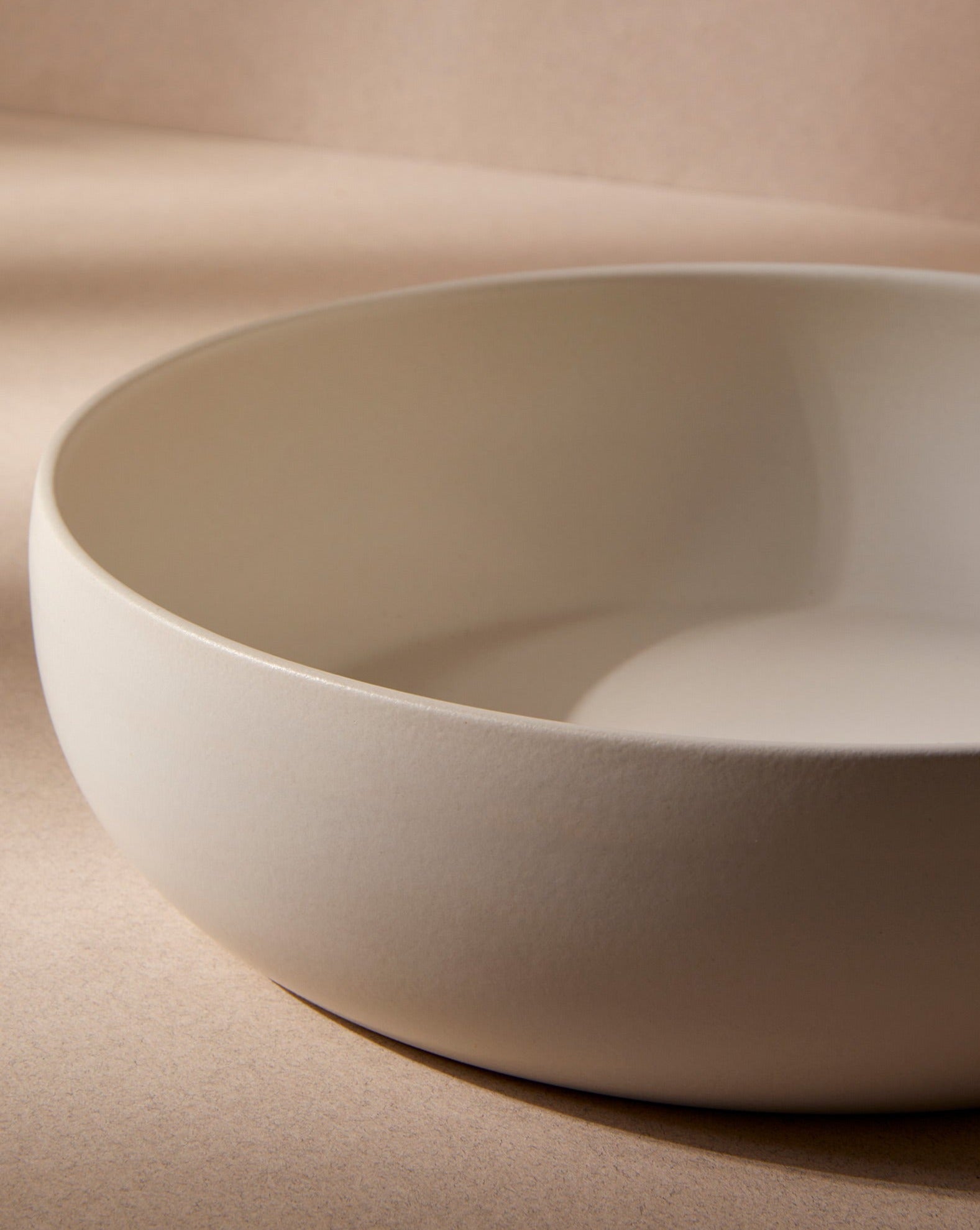 An empty off-white stoneware shallow serving bowl displayed against a plain white background, highlighting its soft, neutral tone and minimalist design.