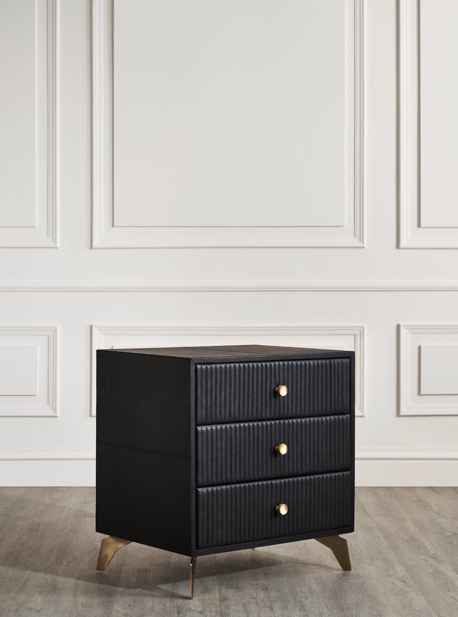 FN-5202-262028_4|Angled view: sleek black leather 3-drawer nightstand, featuring vertical channel tufting and elegant gold tapered legs. Modern furniture.