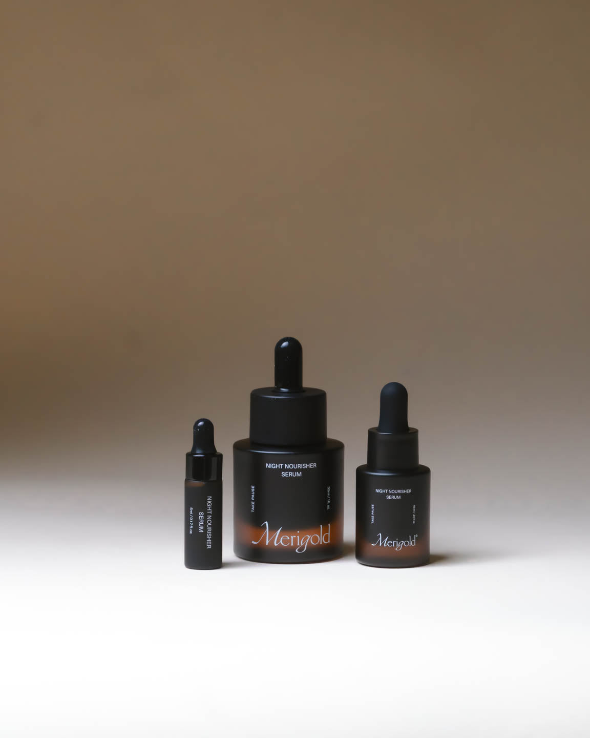 Merigold Night Nourisher Facial Serum shown in amber glass bottles in full size and travel sizes on a neutral background.