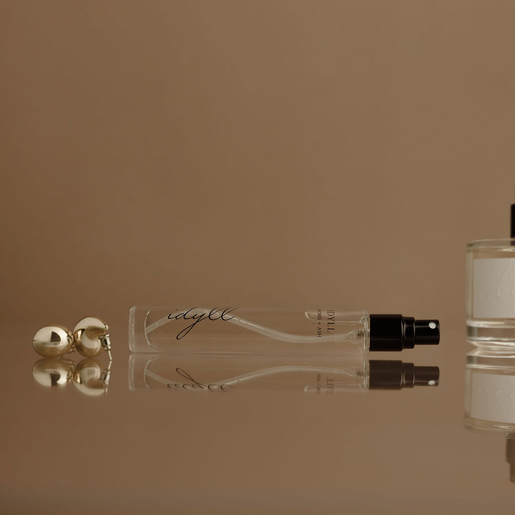 Two perfume bottles and a small container on a reflective surface with a beige background