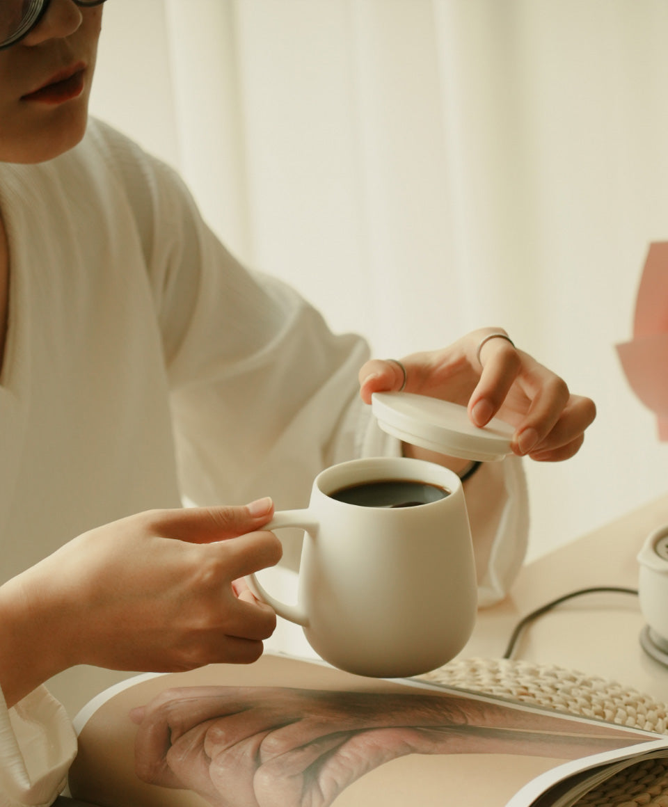 Person holding Ui 3 Self-Heating Ceramic mug 12 fl oz / 355 mL taking off lid with coffee inside