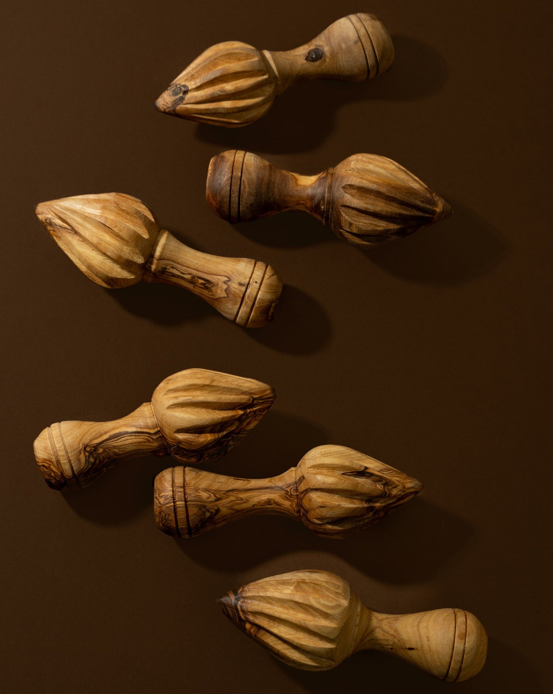 A set of wooden lemon press with natural olive wood patterns, lying on a brown surface.