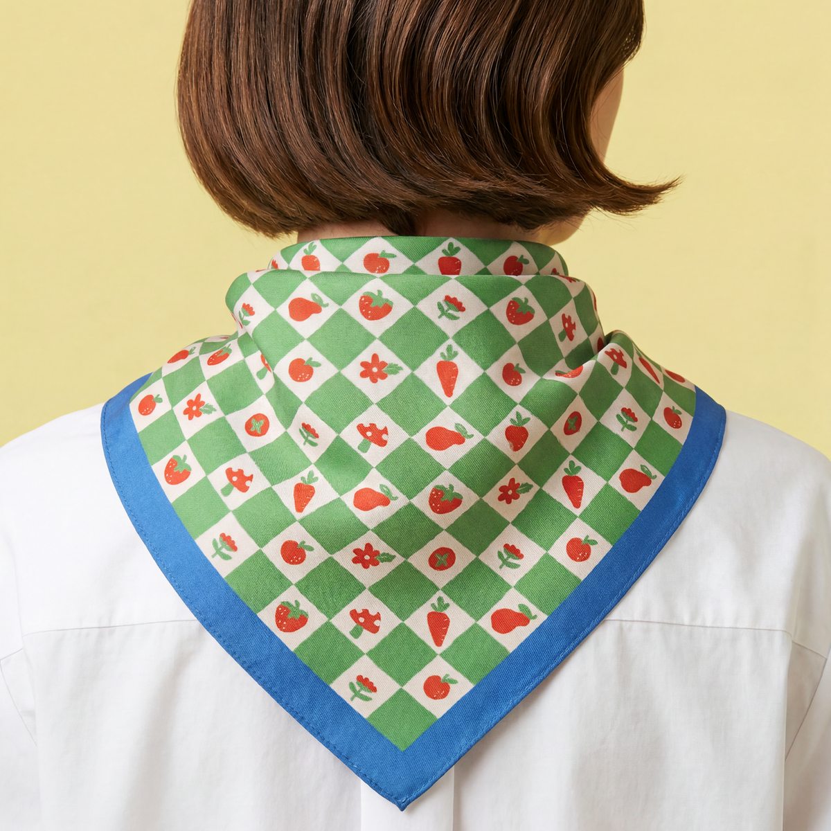 woman wearing a green checkered bandana with orange color fruits, tomato, carrot, orange, mushroom strawberry and white pattern with blue border. 