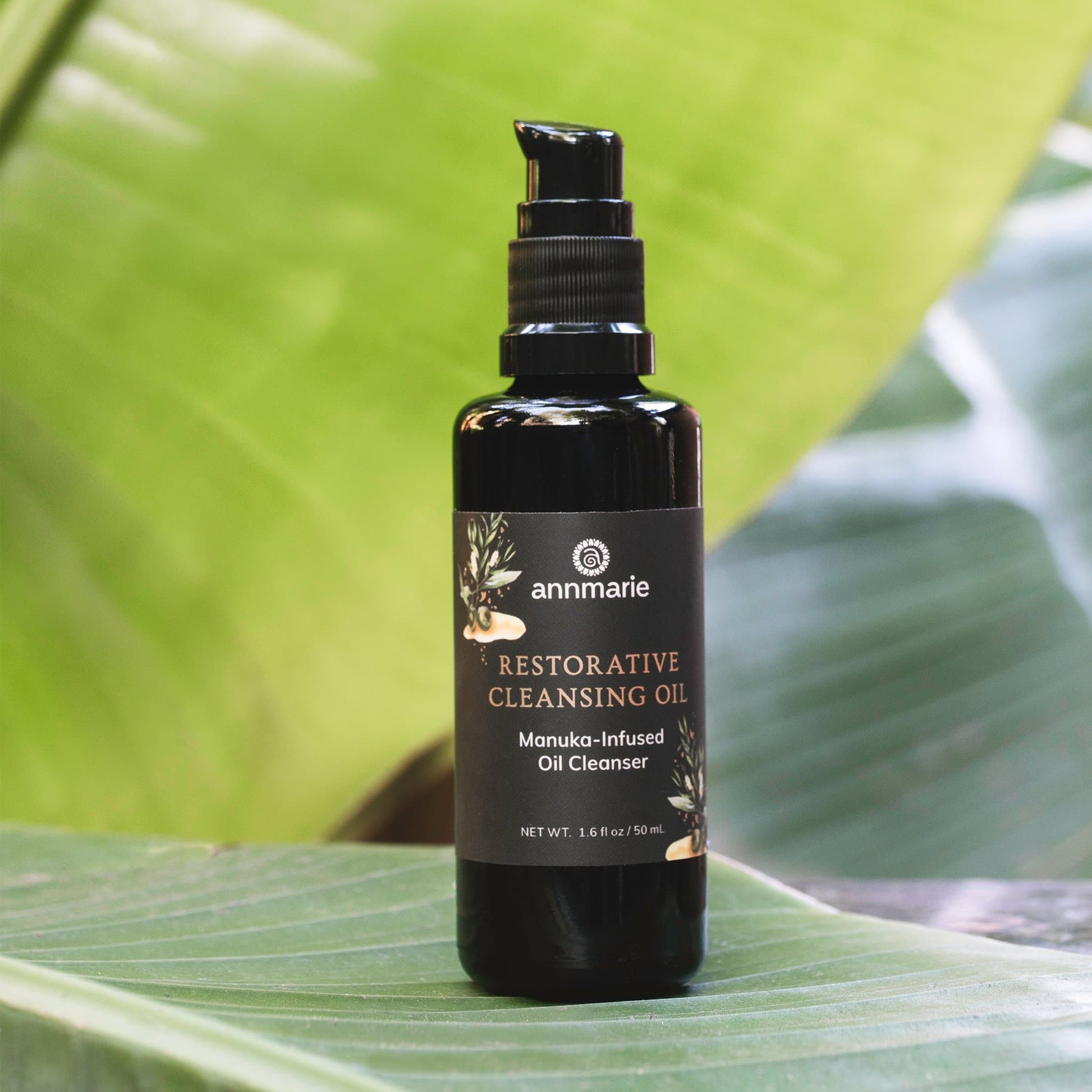 Black bottle of Annmarie Restorative Cleansing Oil on a green leaf background