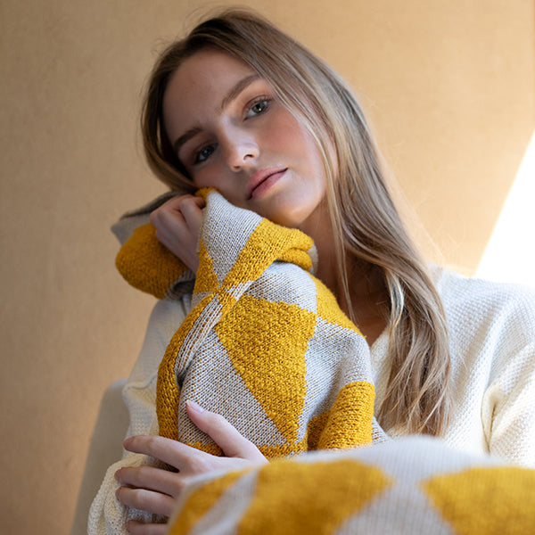 Woman holding a soft yellow and white knitted blanket against her face. 