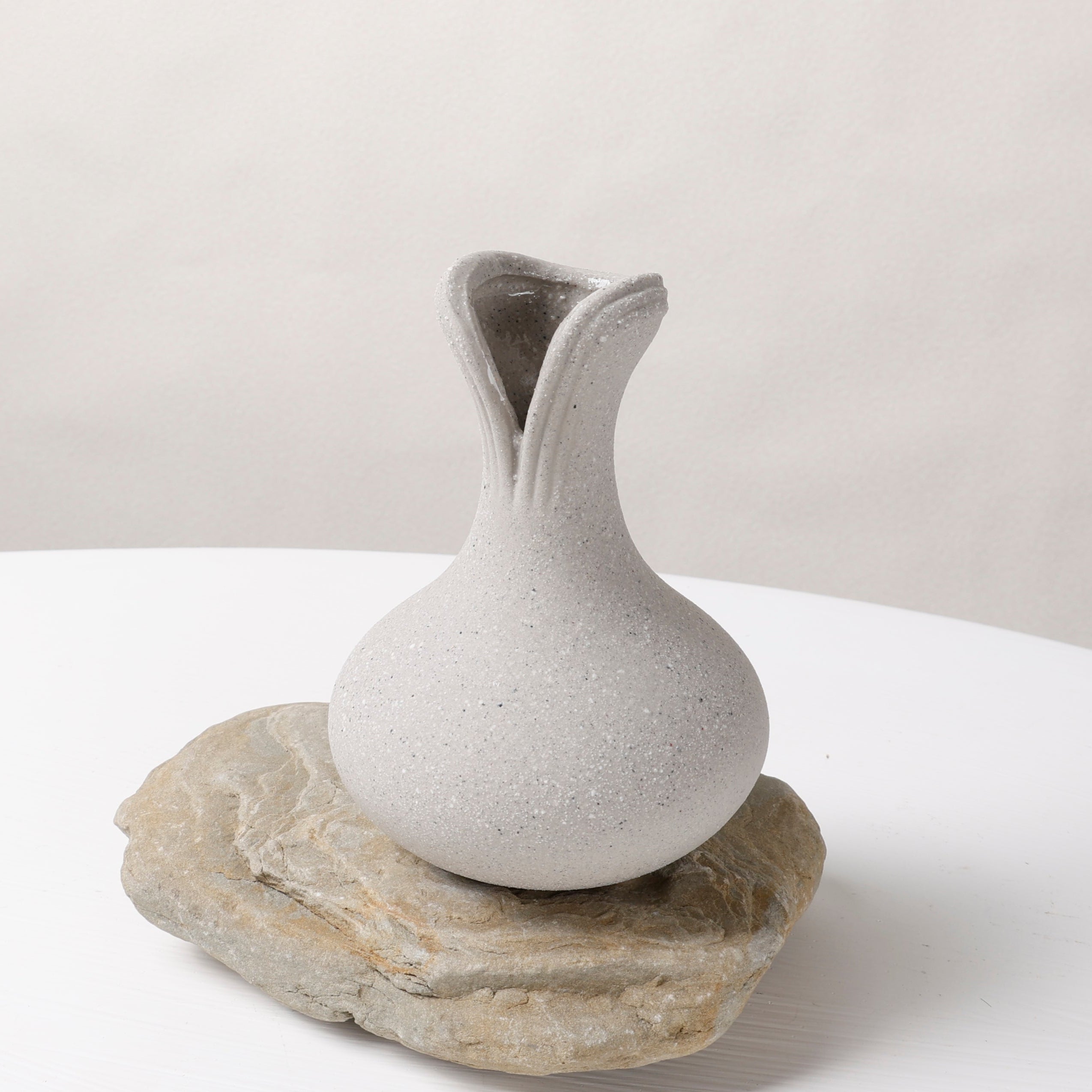 White ceramic vase on a natural stone base against a plain background