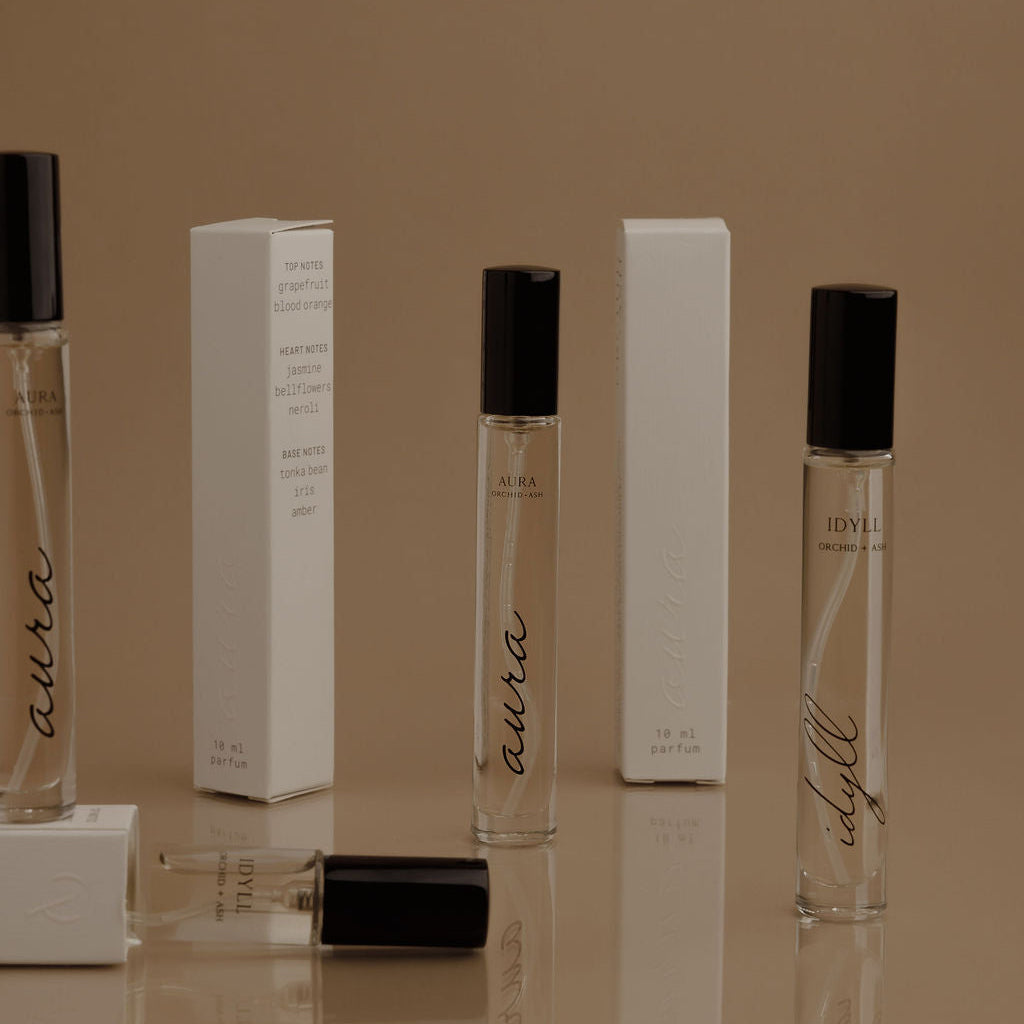 Perfume bottles with 'aura' branding on a reflective surface against a brown background
