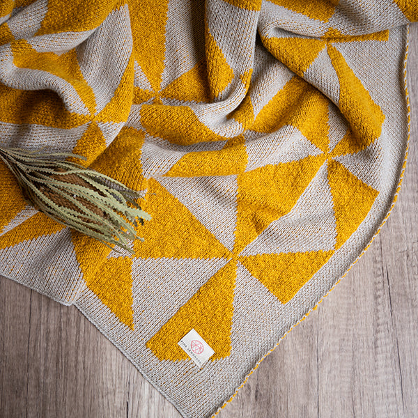 Textured cotton throw blanket with geometric bright yellow and white patterns on a wooden surface.
