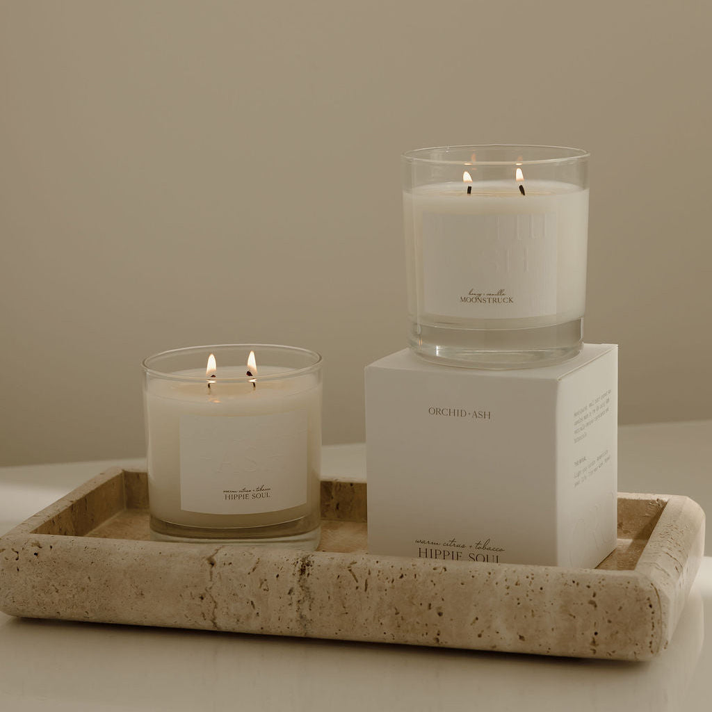 Two lit candles on a tray with a box labeled 'The White Company' against a neutral background.