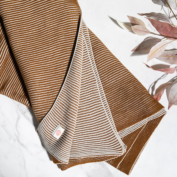 Copper and white striped throw blanket on a white surface with floral decorations.