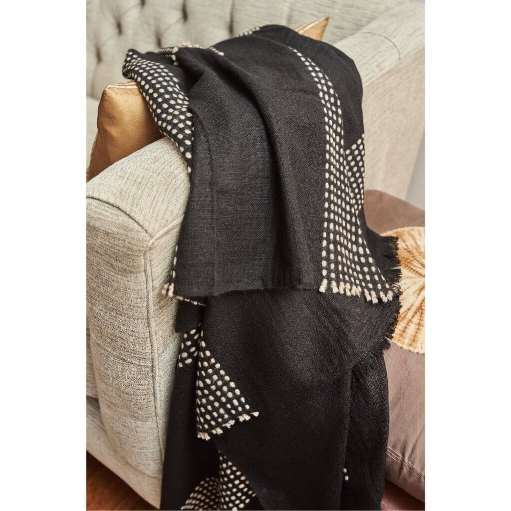 Walnut Black Yak With Hand Knotted Merino Stripes Handloom Throw draped over a couch, showcasing intricate design.