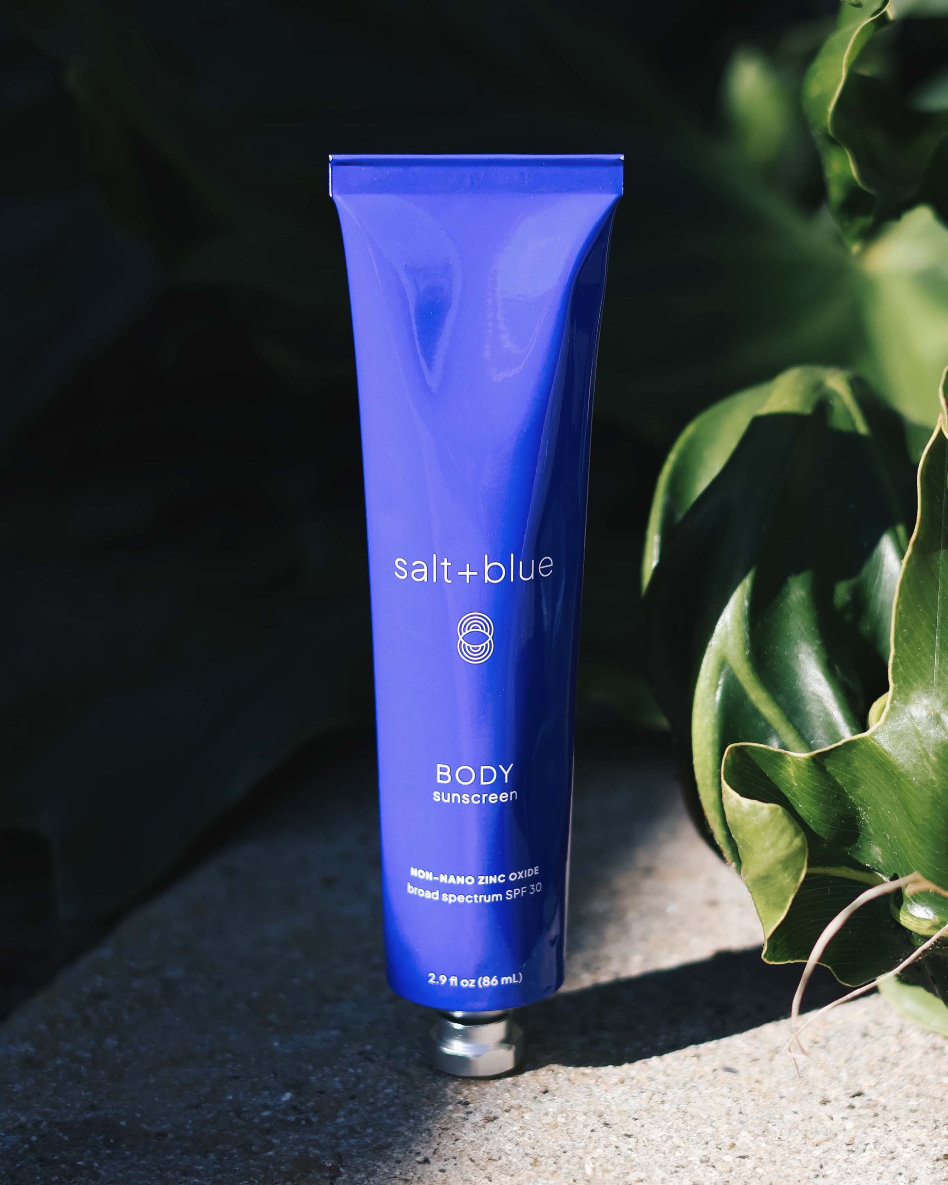 Blue tube of salt+blue sunscreen on a dark background with green leaves