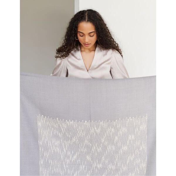 Woman showcasing the Flo Gray Textured Handloom Merino Throw with intricate designs and luxurious texture.