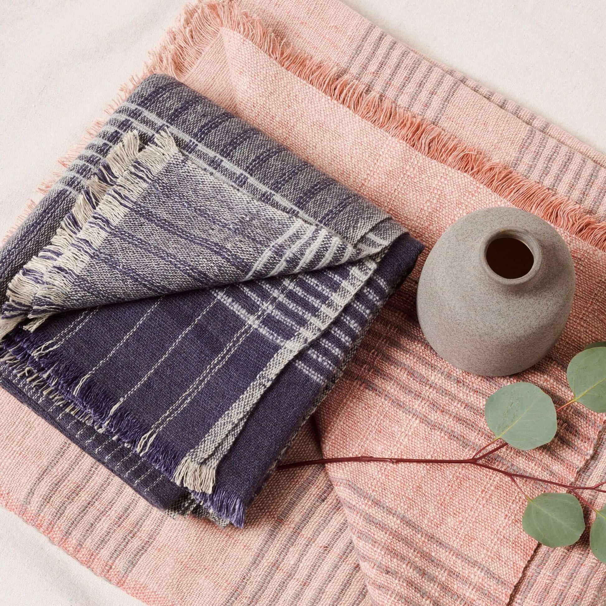 Alloy Dark Blue Stripes Pattern Soft Merino Linen Handloom Throw folded with a decorative vase and greenery.