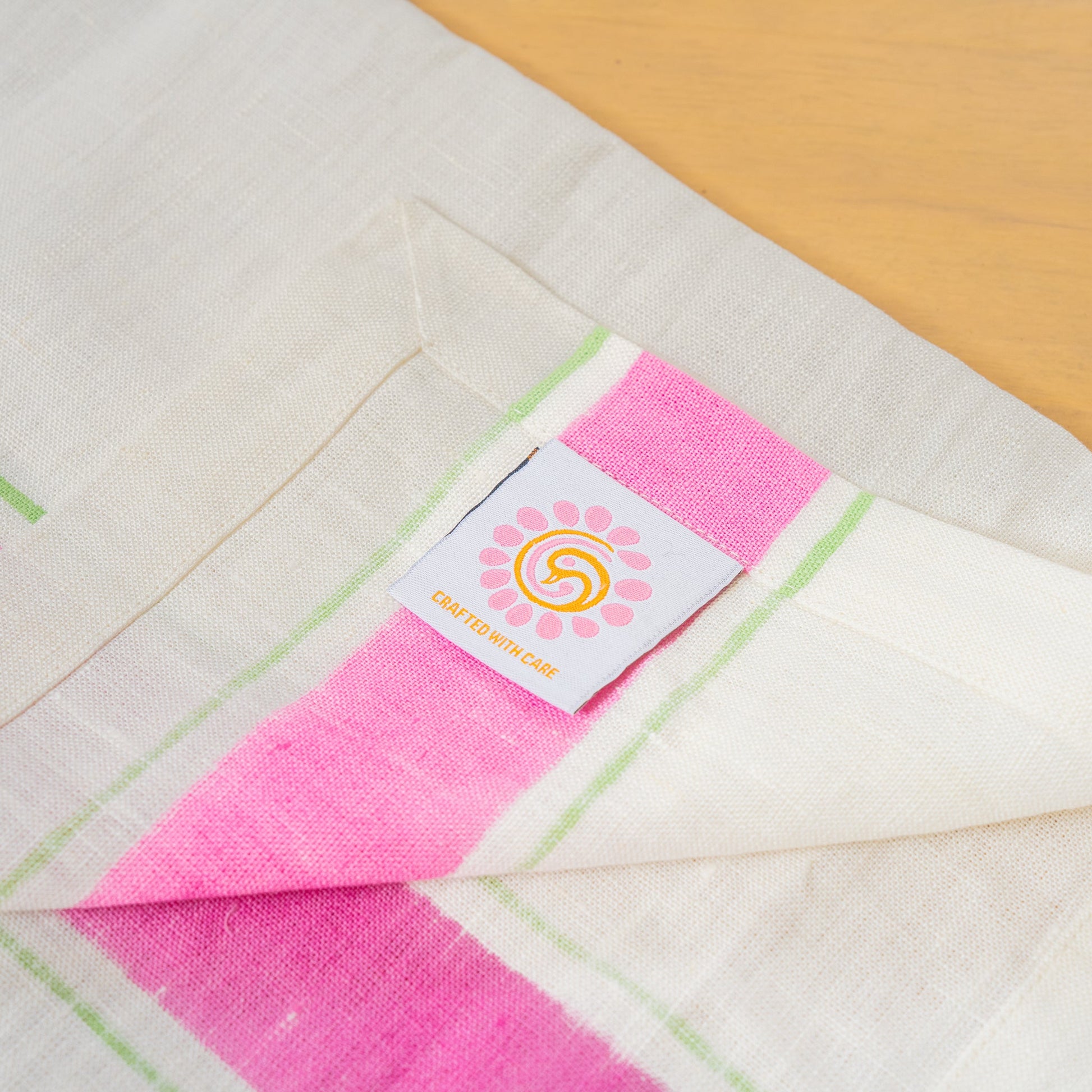 Hand printed linen napkins in pink, folded  with the peacock palette label laid out on a table