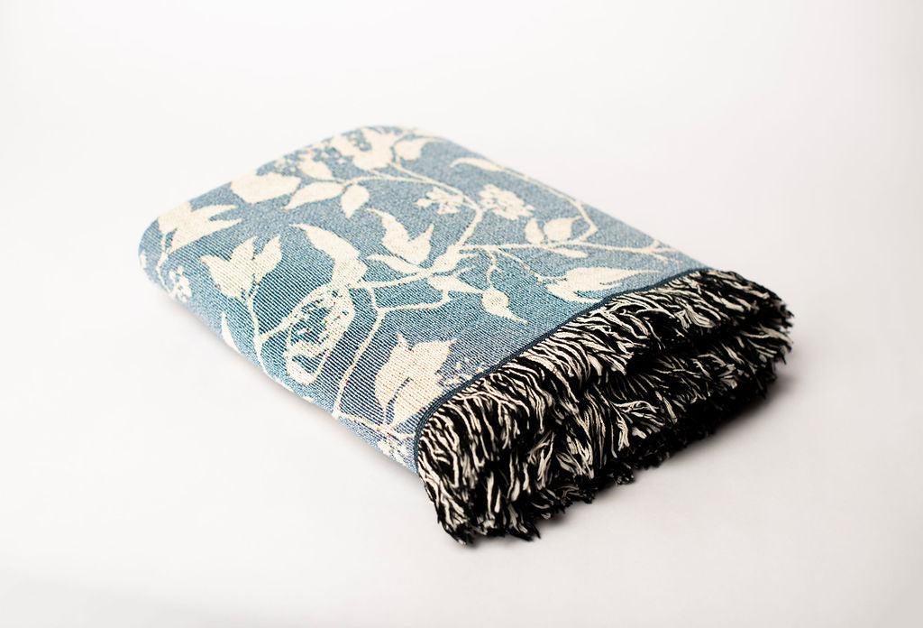 Folded Wren Chambray blue bird and botanical jacquard woven throw blanket with black and cream fringe
