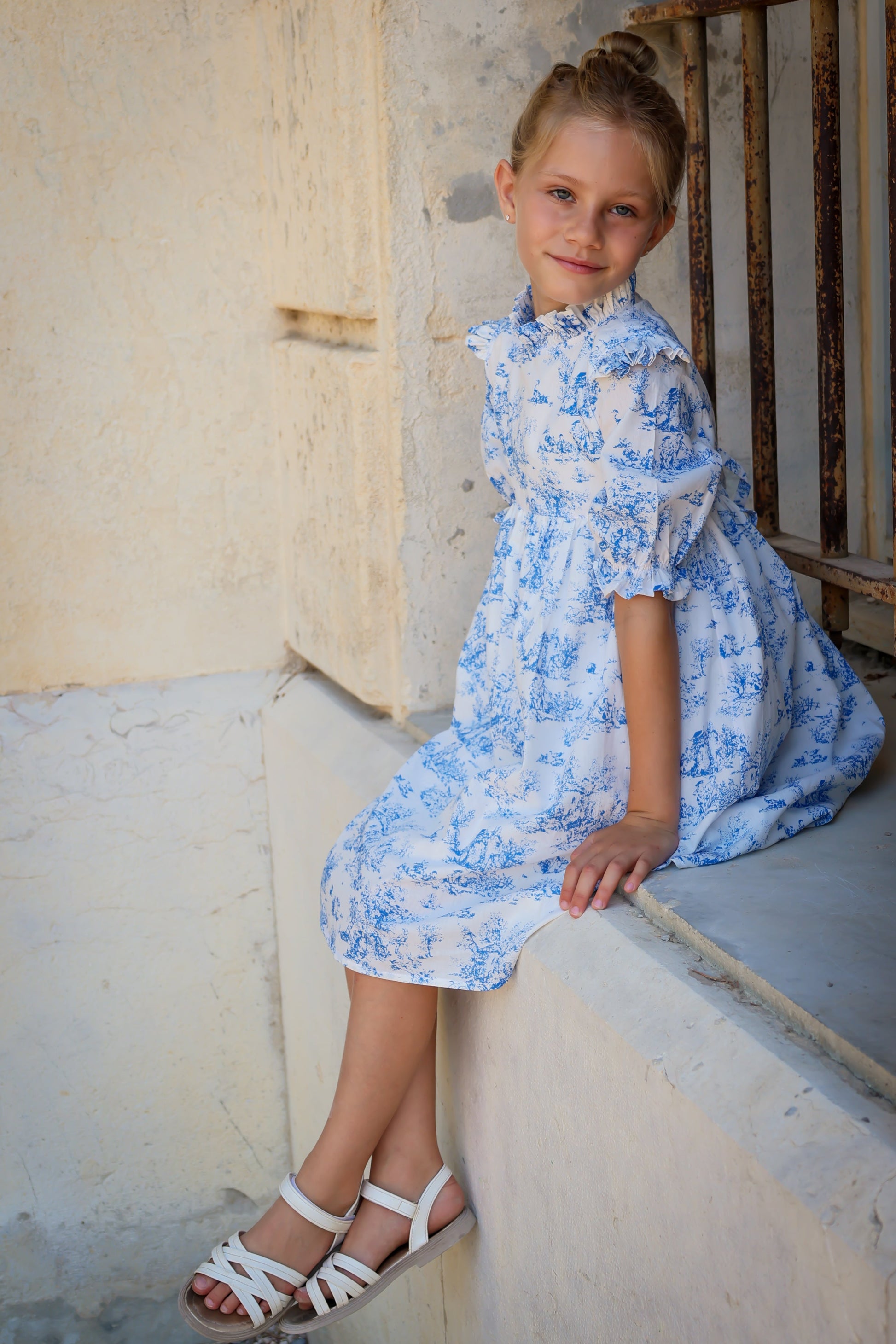 Young girl in a blue floral dress sitting on a step.