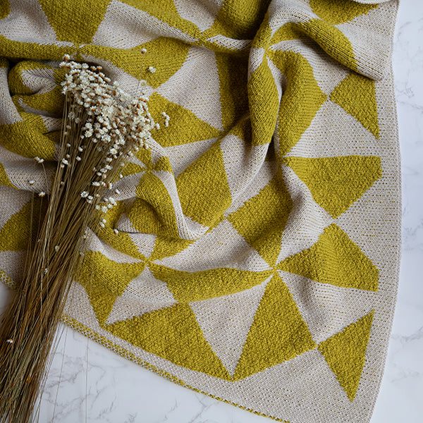 Bush green and white geometric patterned throw blanket with dried flowers on a marble surface.