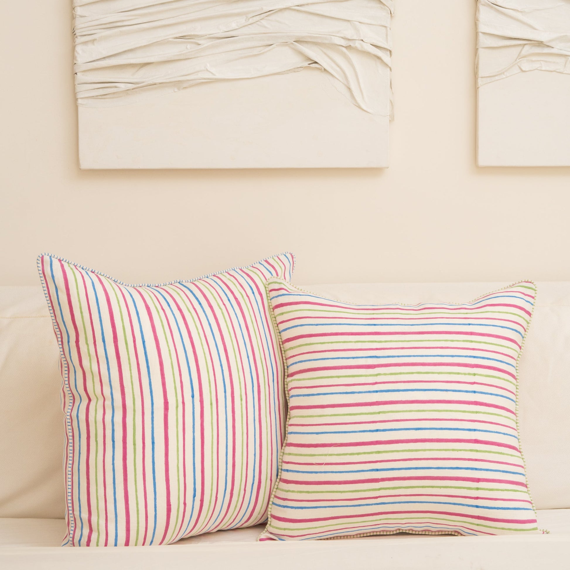 Two Striped with pink, blue, and green lines hand block printed linen pillow cover s in natural dyes  placed on a beige sofa with abstract art in the background.