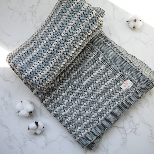 Light gray and white striped organic cotton knitted throw on a marble surface with cotton buds.