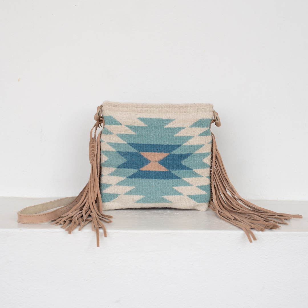 Woman carrying Handwoven fringe crossbody bag with abstract Zapotec diamond design in soft spring colors; features adjustable leather strap and two internal pockets