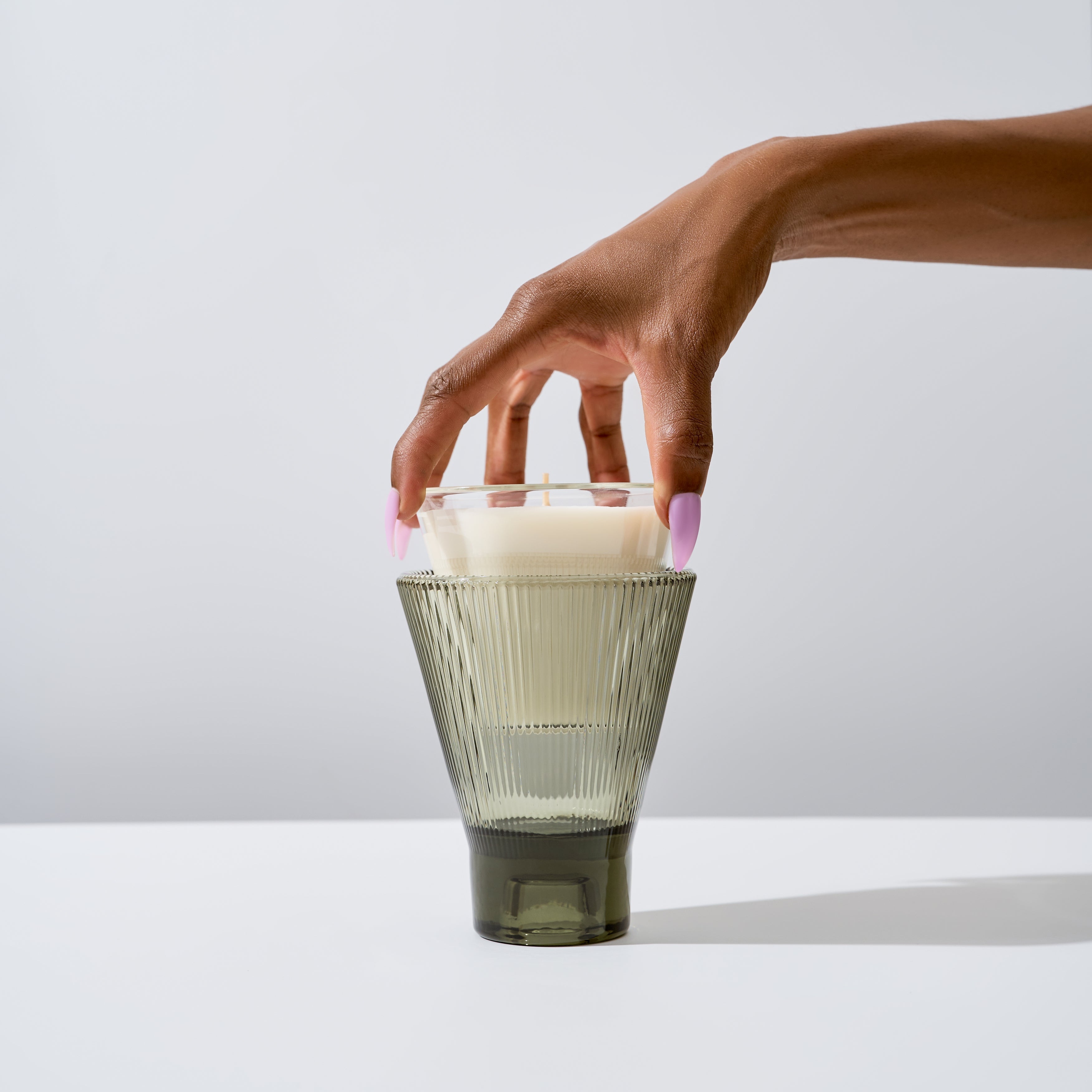 Hand placing a candle inside a glass holder on a white surface with a light gray background