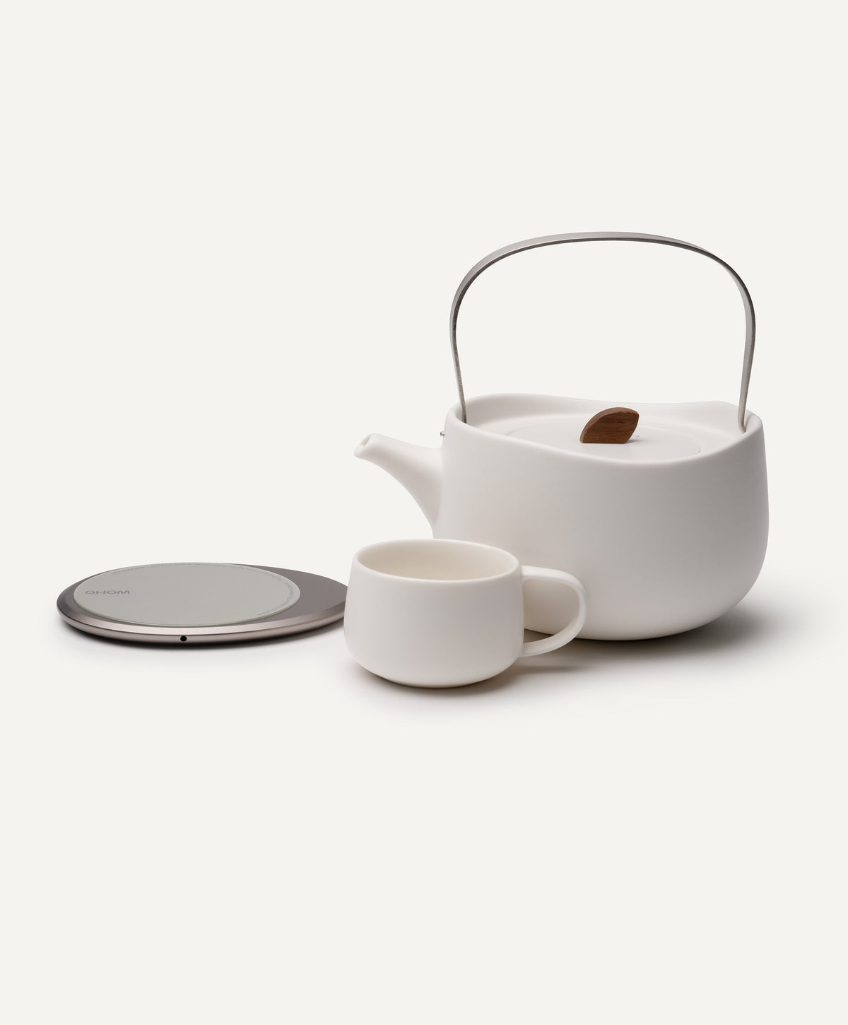 Leiph self-heating ceramic teapot 20 fl oz / 600 mL in Jasmine White with tea cup beside OHOM Pad 3 charging base