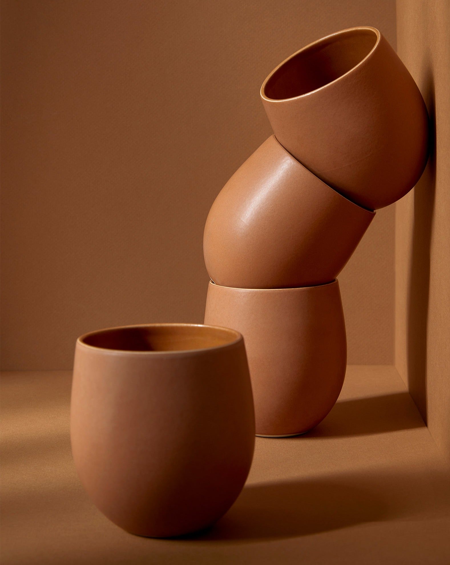 A set of beige stoneware coffee and tea cups with a matte finish, displayed in an artistic manner against a neutral background.