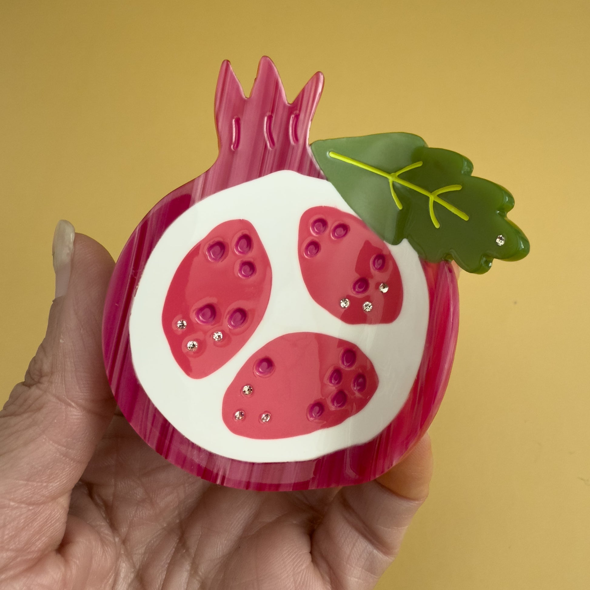 Decorative pomegranate hair claw with a green leaf. Don't let this tough exterior fool you! Beneath its rosy glow lies a treasure chest of tiny, ruby-red jewels, each one a delightful explosion of sweet-tart goodness.

Pomegranate hair claw season is here and we can help but wearing it too!