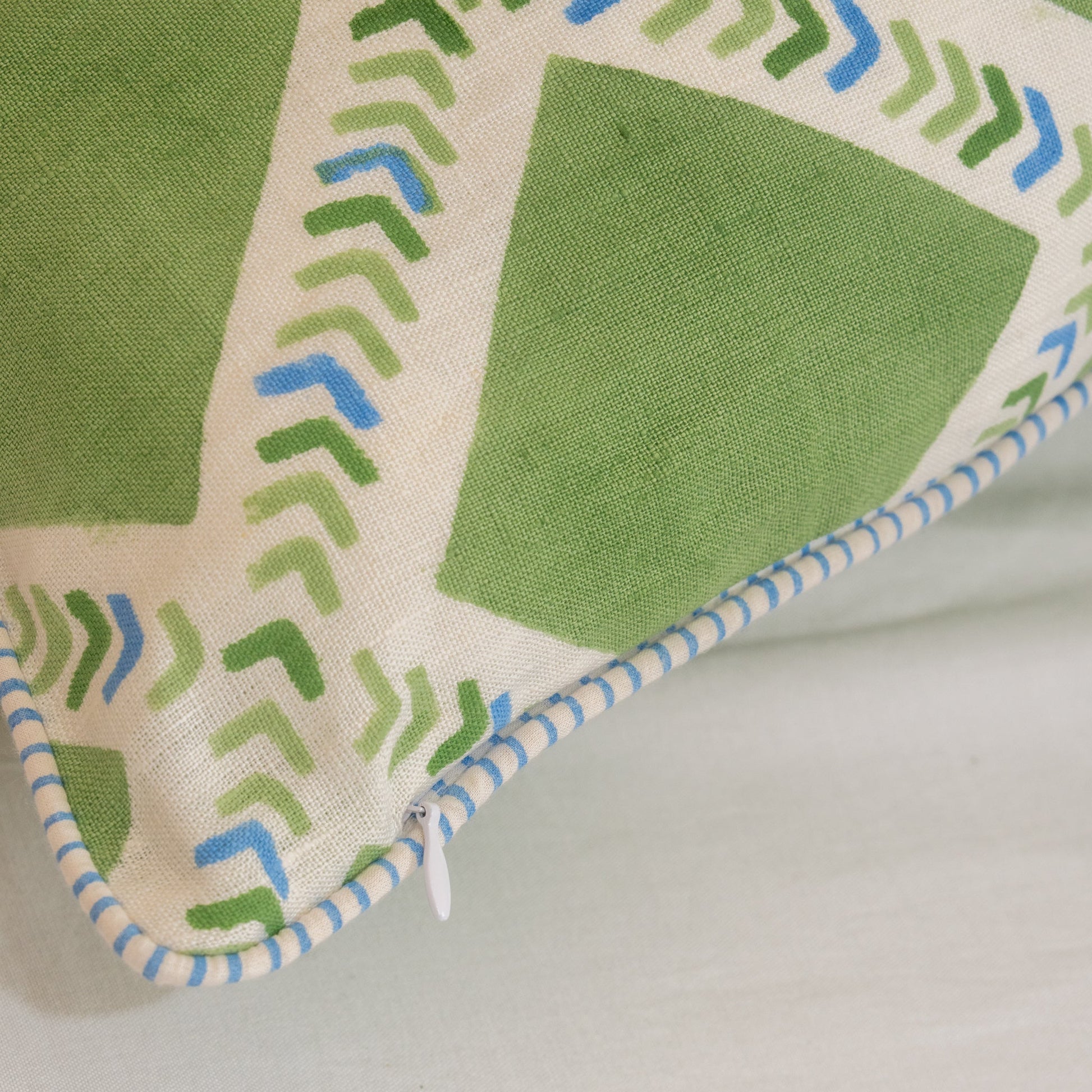 Close-up of a Hand block printed linen pillow cover with interlocking geometric green and blue chevron  print in natural dyes placed on a light gray background