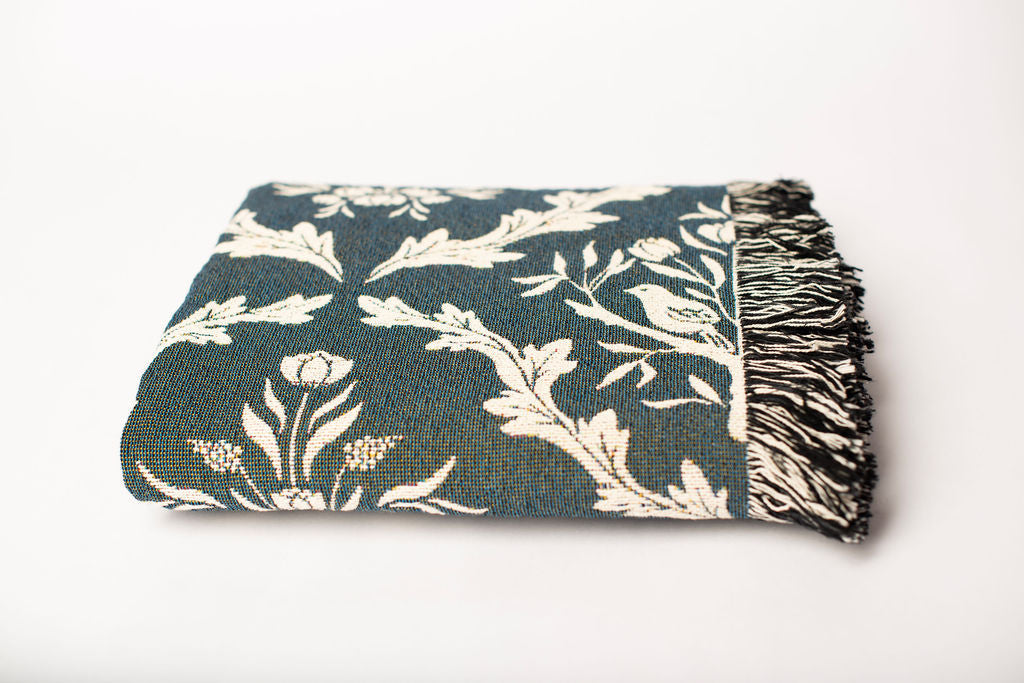Front view of folded teal and cream floral woven throw blanket with fringe