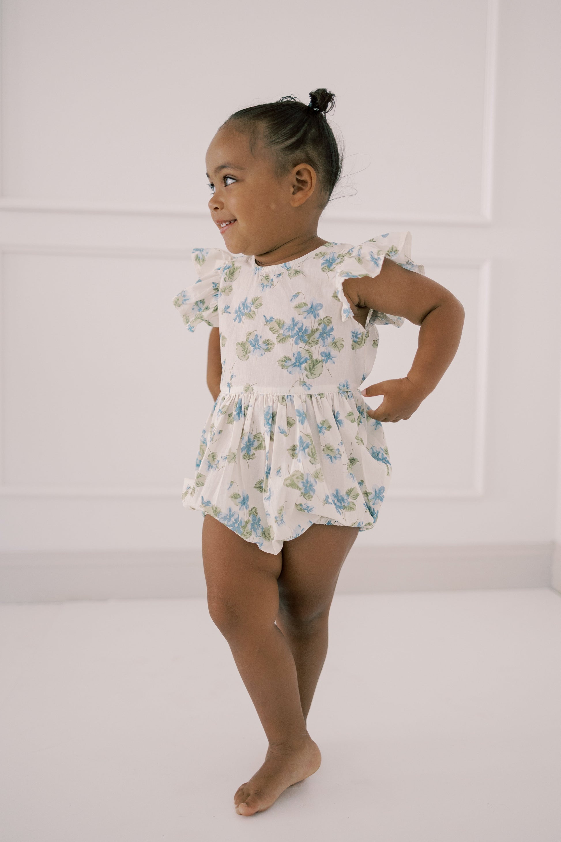 Young girl wearing a floral romper against a white background