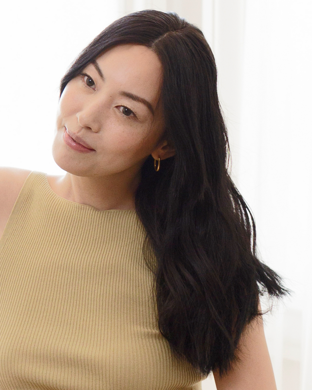Woman with long dark hair wearing a beige top against a white background