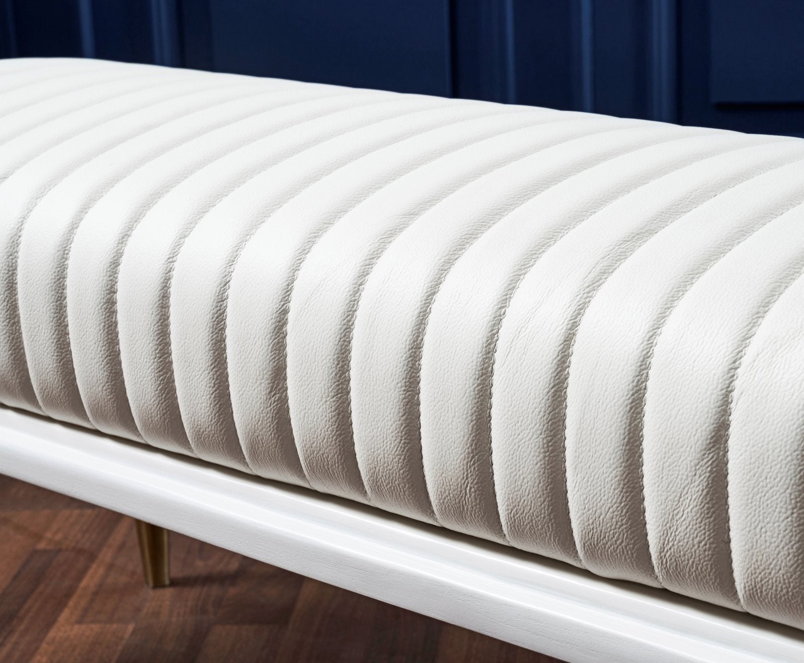 FN-5203-601618_6|White leather channel tufted bench with elegant gold-tipped legs on dark wood floor, modern luxury furniture.