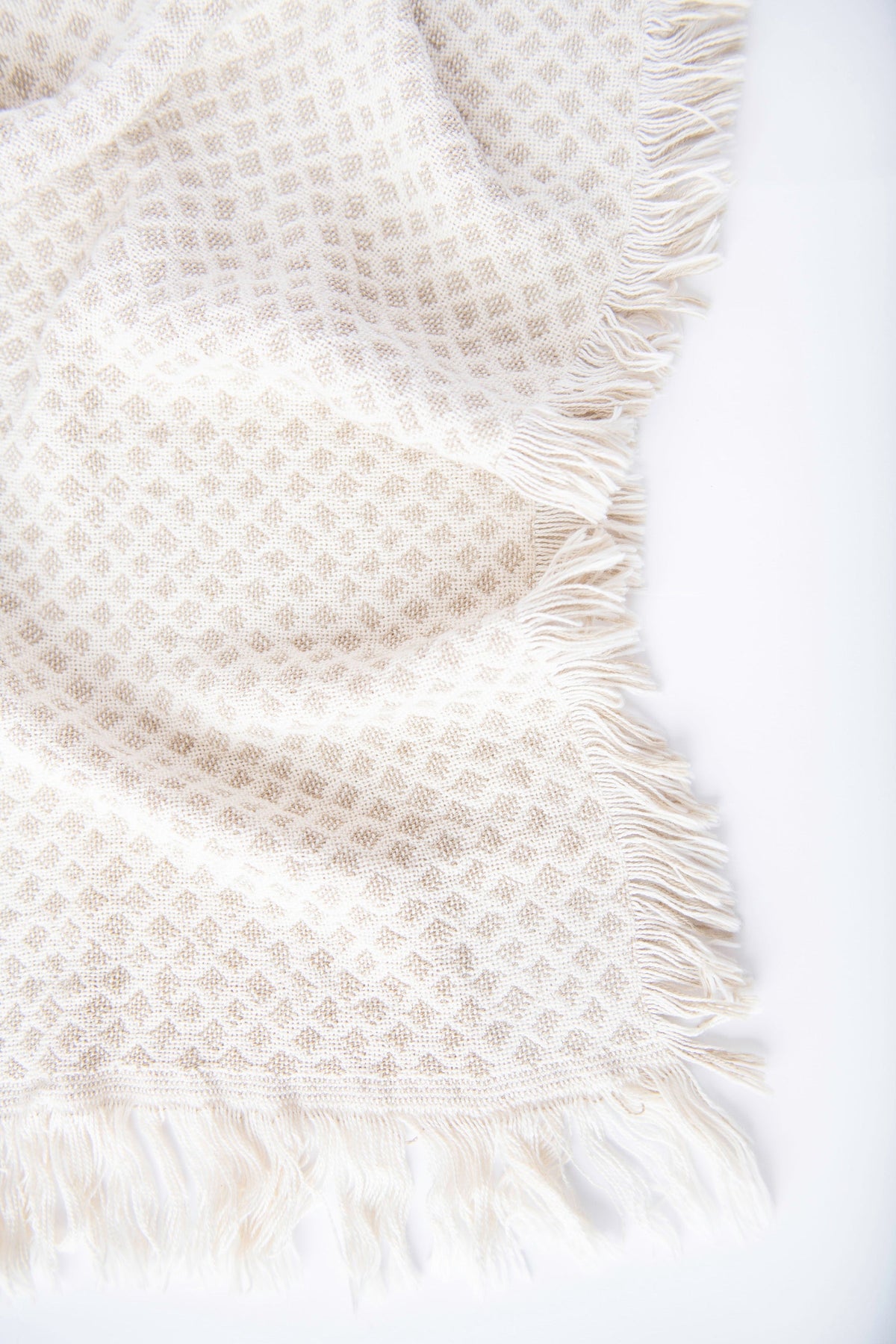 Close-up of Rowan cream and beige diamond-patterned woven cotton throw with neutral fringe