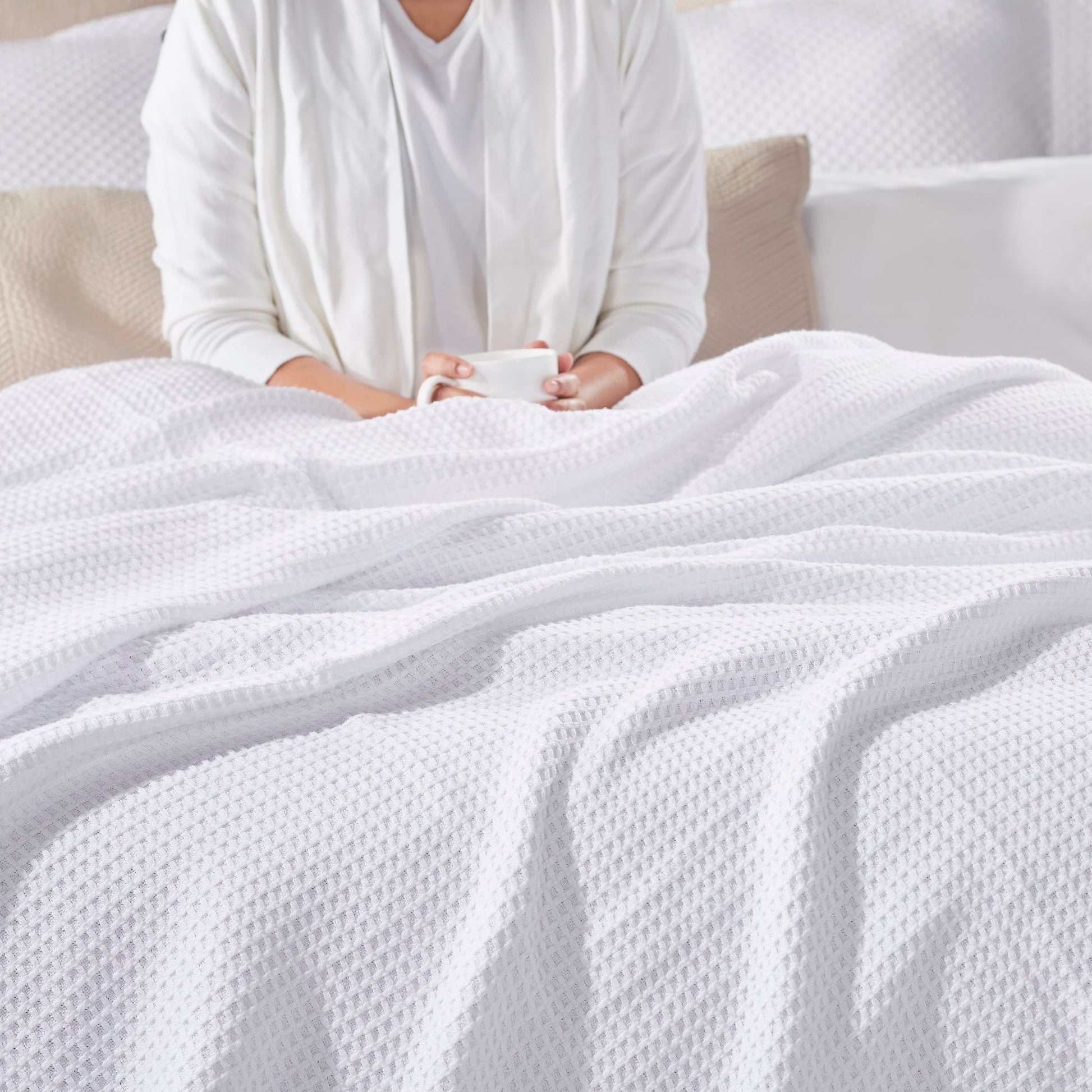 BL-855-9496_2|Plush white waffle weave blanket providing comfort for a person relaxing in bed, holding a mug for a cozy morning.