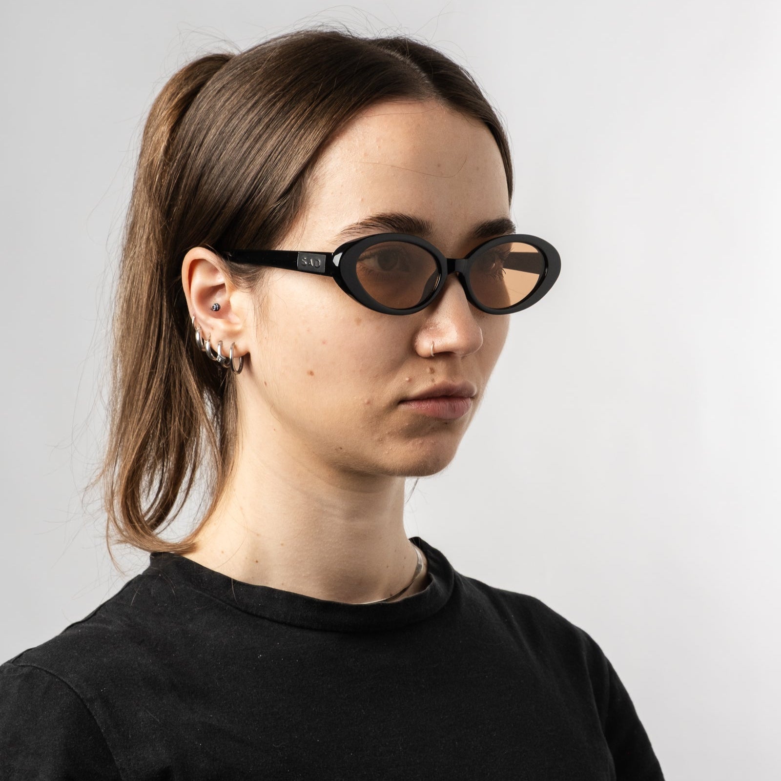 Female wearing Sad Eyewear Bloom oval sunglasses in black with tinted bronze lenses