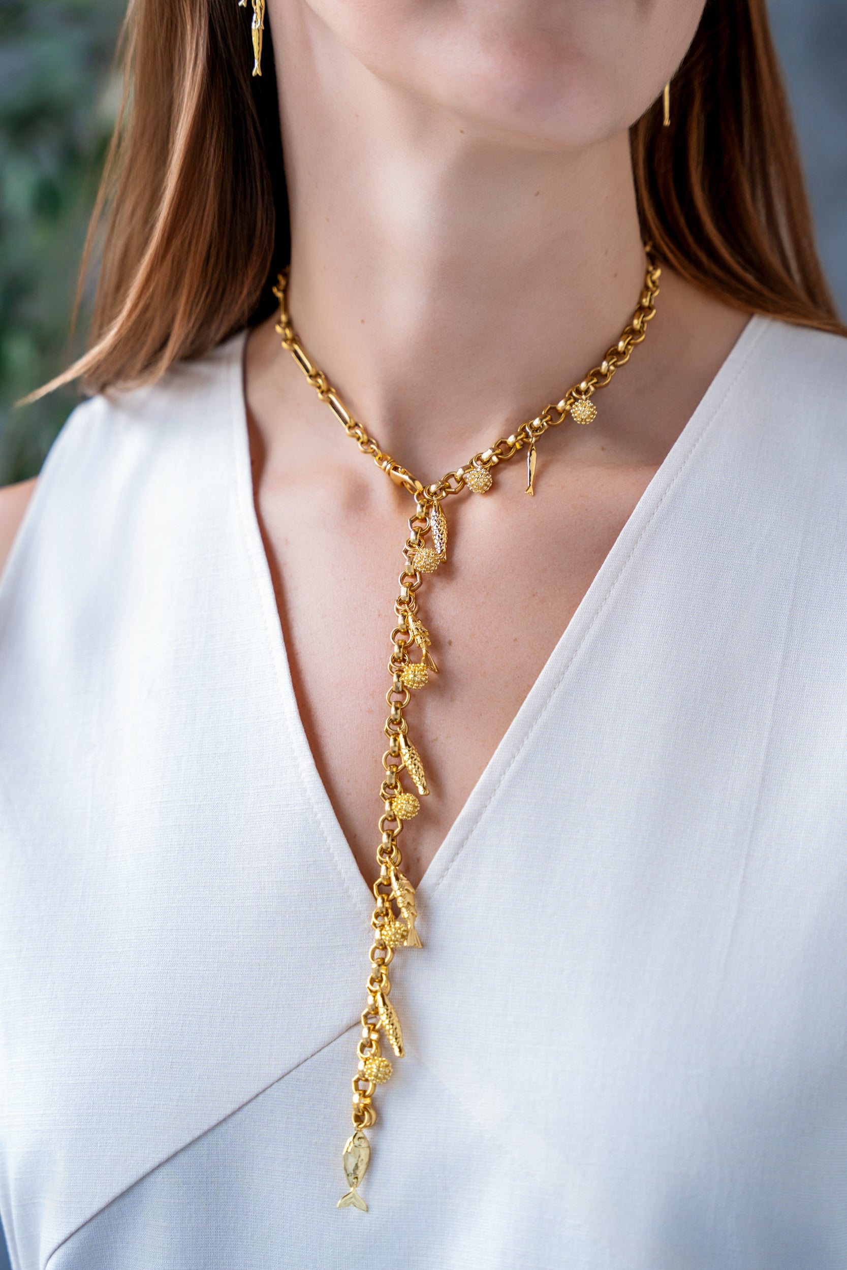 Convertible gold fish charm necklace with dangling fish and textured bead charms worn as both a lariat and classic chain necklace.