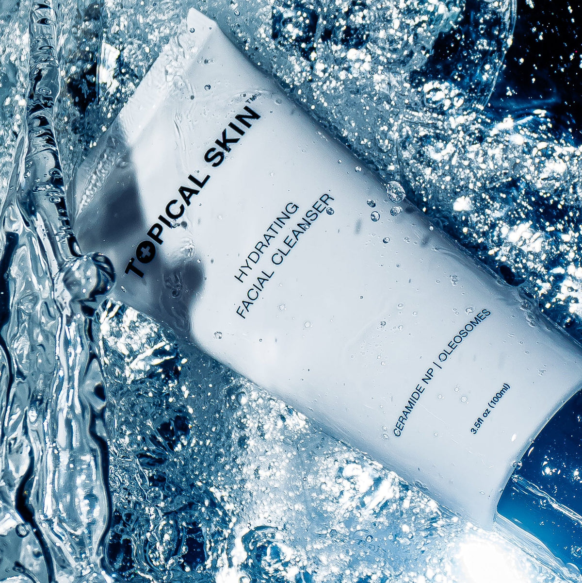 A white tube of TOPICAL SKIN Hydrating Facial Cleanser surrounded by splashing water and ice, with blue-toned lighting and visible product text.
