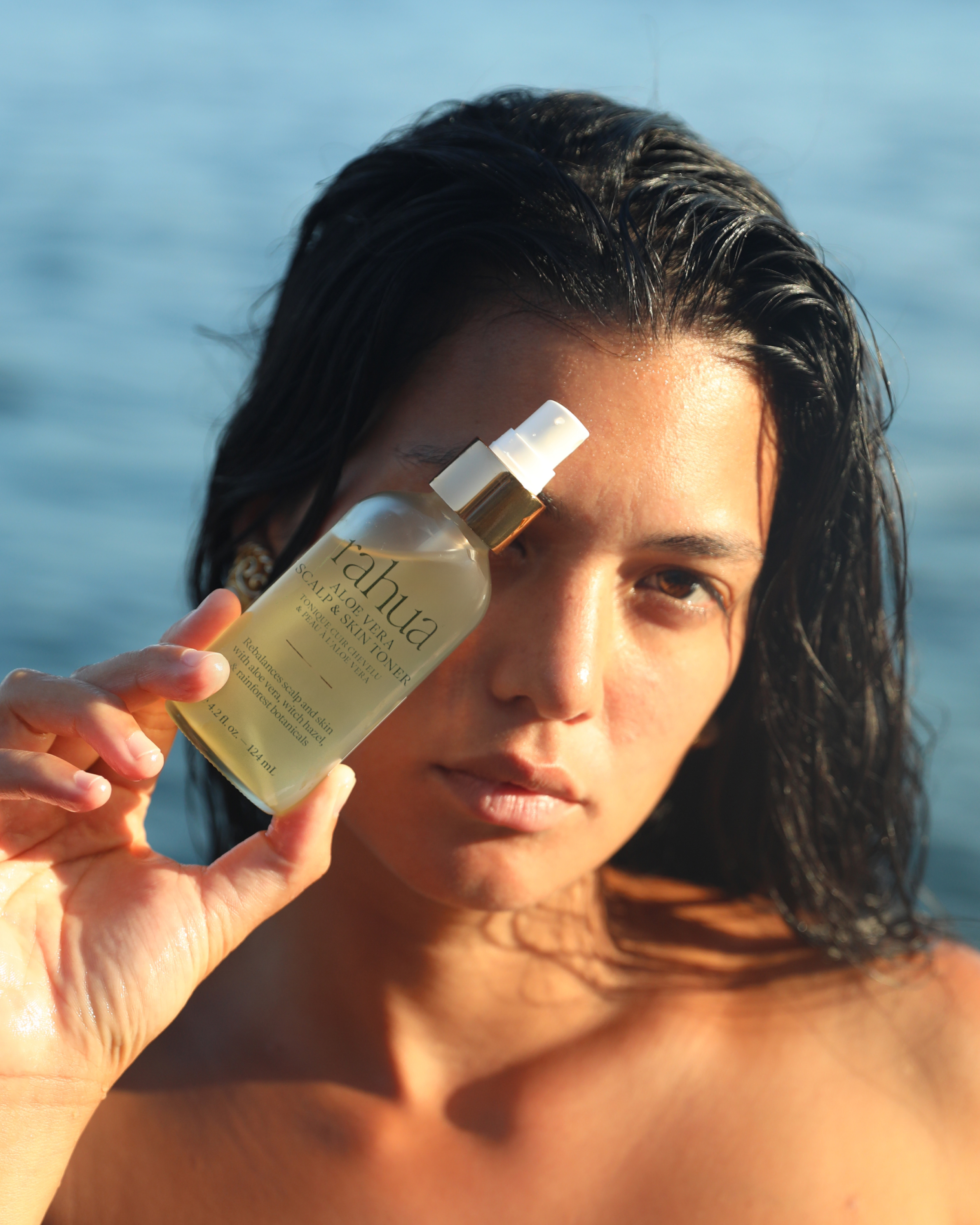 Woman applying sunscreen with a bottle labeled 'Vaha' by the ocean.|variant:42-oz