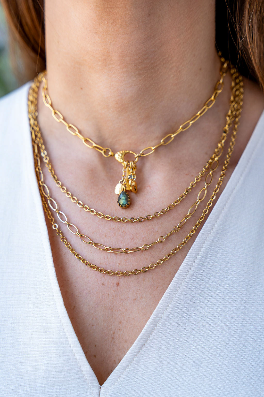 Gold chain necklace with a front clasp and dangling charms including a teardrop labradorite and textured gold talismans.