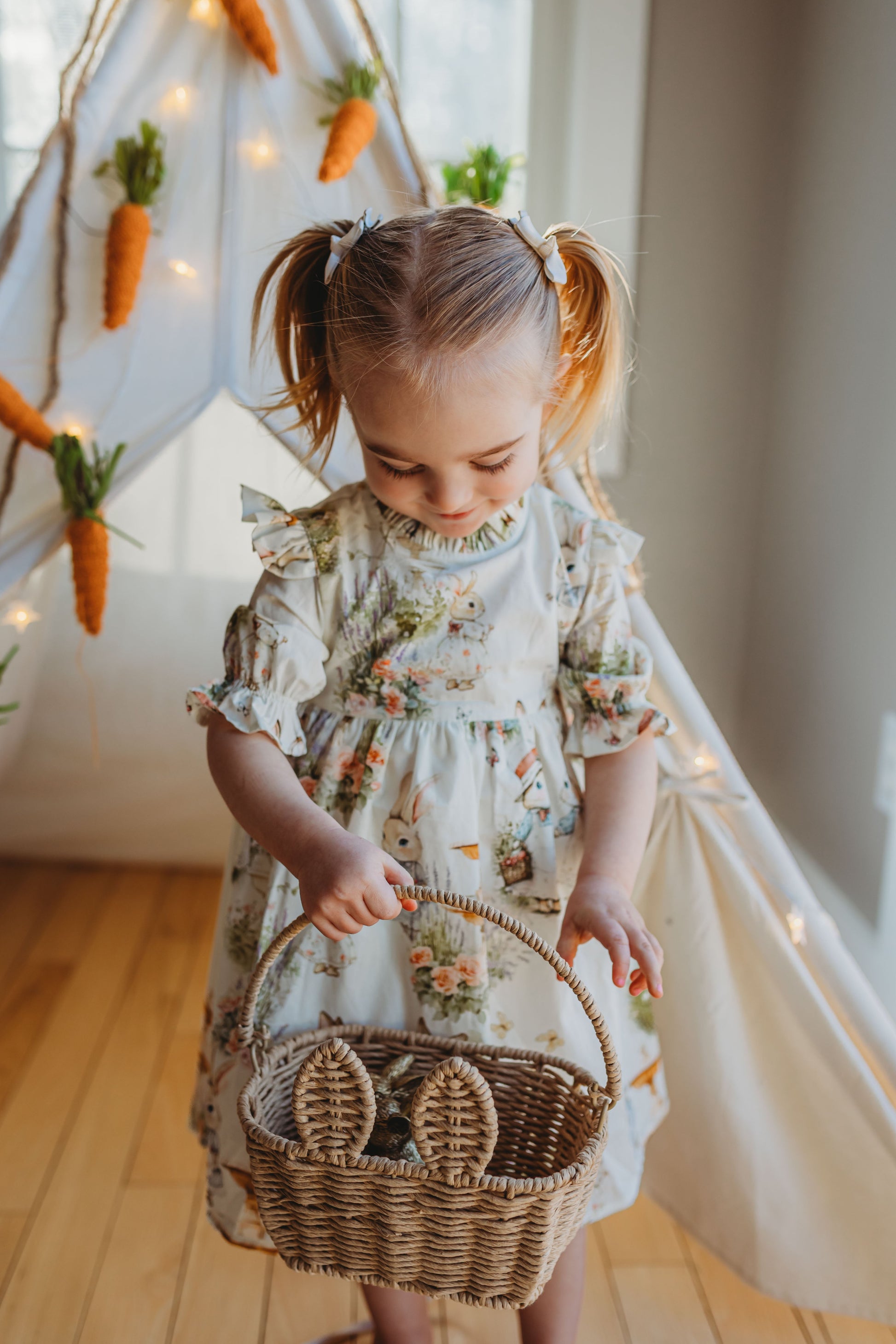 Child in a floral dress holding a basket with Easter decorations in the background.