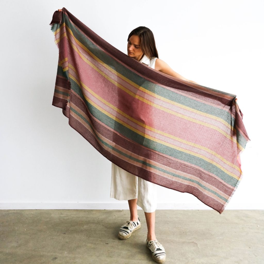 Woman holding the Barque Clay Modern Artisan Striped Soft Merino Handwoven Scarf against a white background.